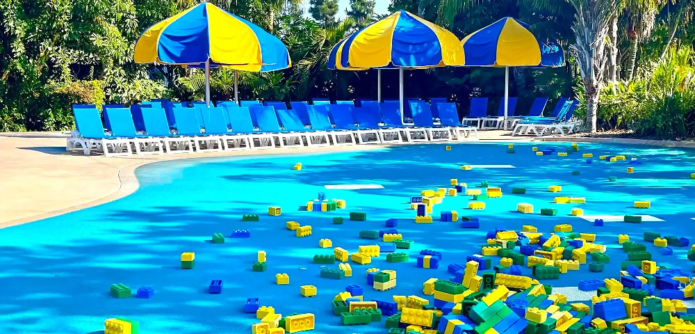 Commercial pool area with blue Jamaica Beach Chaises and colorful umbrellas creating a fun, family-friendly pool deck design at Legoland.